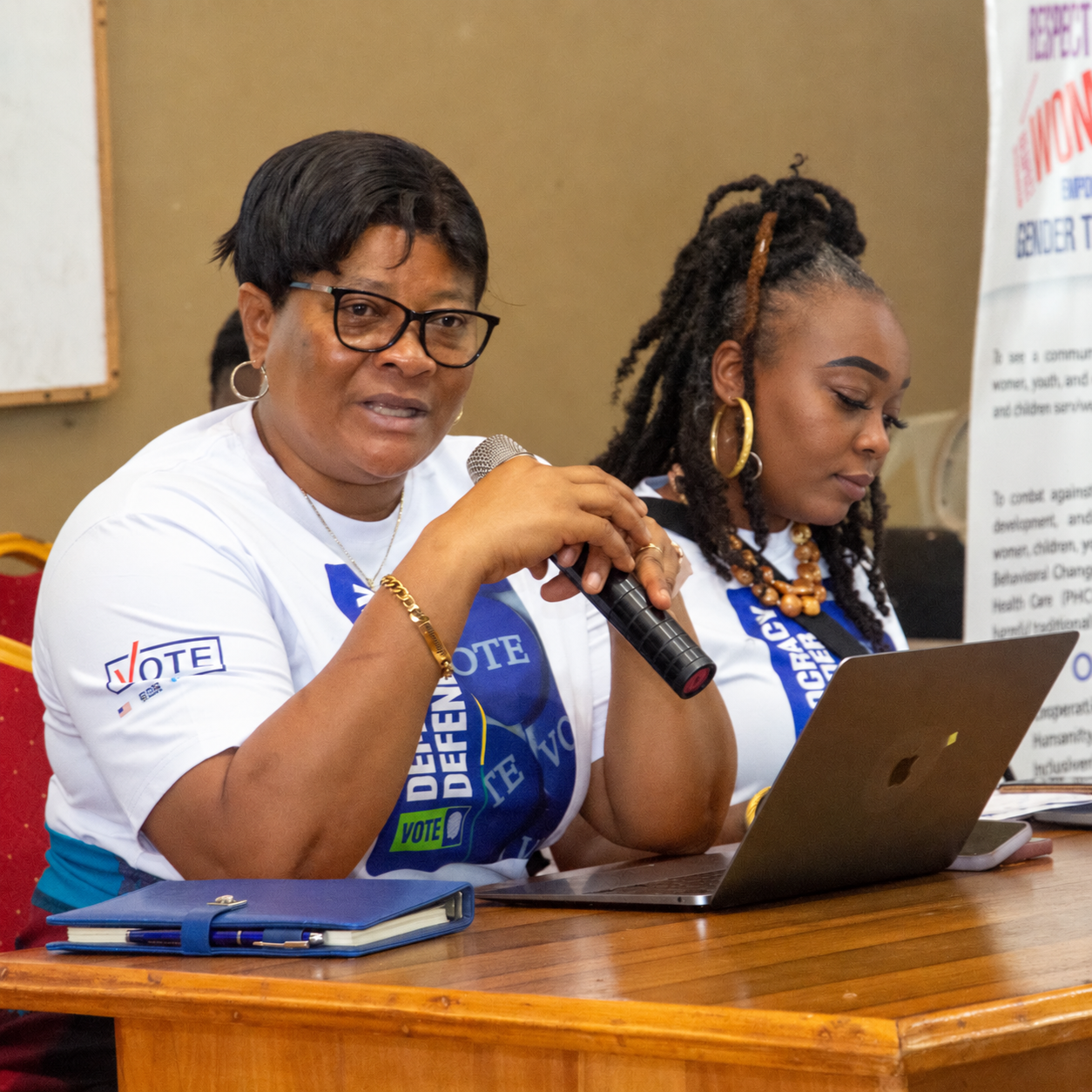Marsita at a laptop alongside a fellow facilitator speaking into a microphone in Ghana